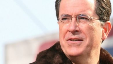 Stephen Colbert wearing glasses and smiling at the camera