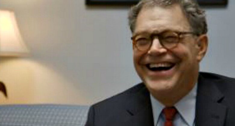 Al Franken wearing a suit and tie smiling at the camera