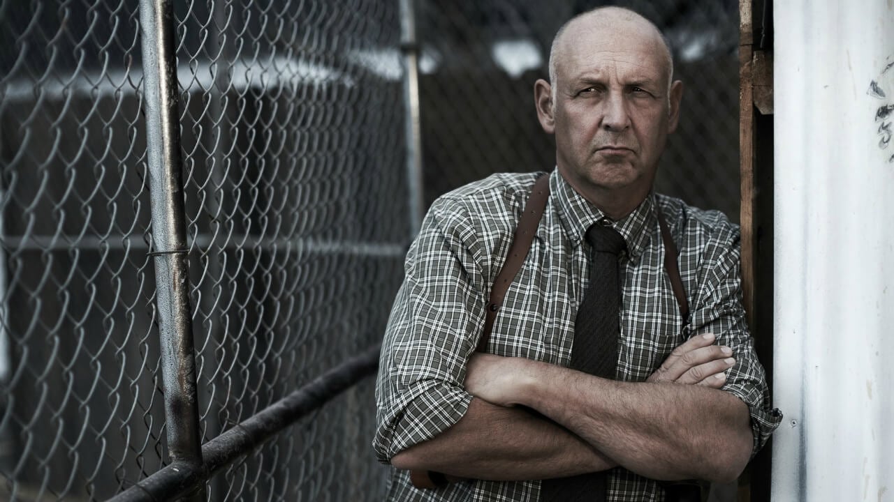 Nick Searcy sitting in front of a fence