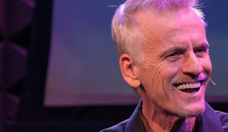 Rob Paulsen wearing a purple shirt and smiling at the camera