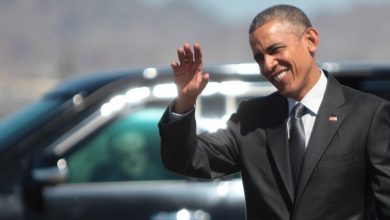 Barack Obama wearing a suit and tie talking on a cell phone