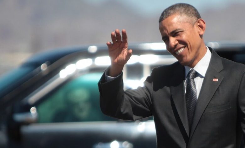 Barack Obama wearing a suit and tie talking on a cell phone